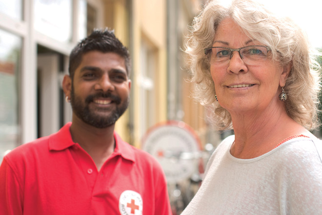 Ein DRK-Mitarbeiter im roten Poloshirt und eine Frau mit grauem Haar Brille